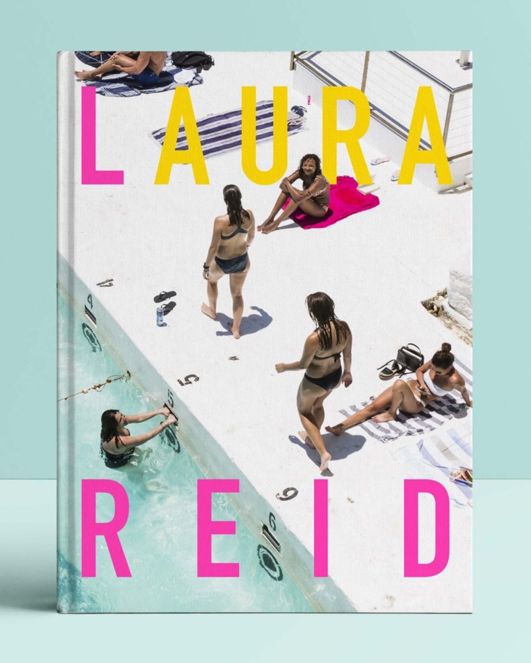 Book with people and swimming pool on the cover and Laura Reid in yellow and pink