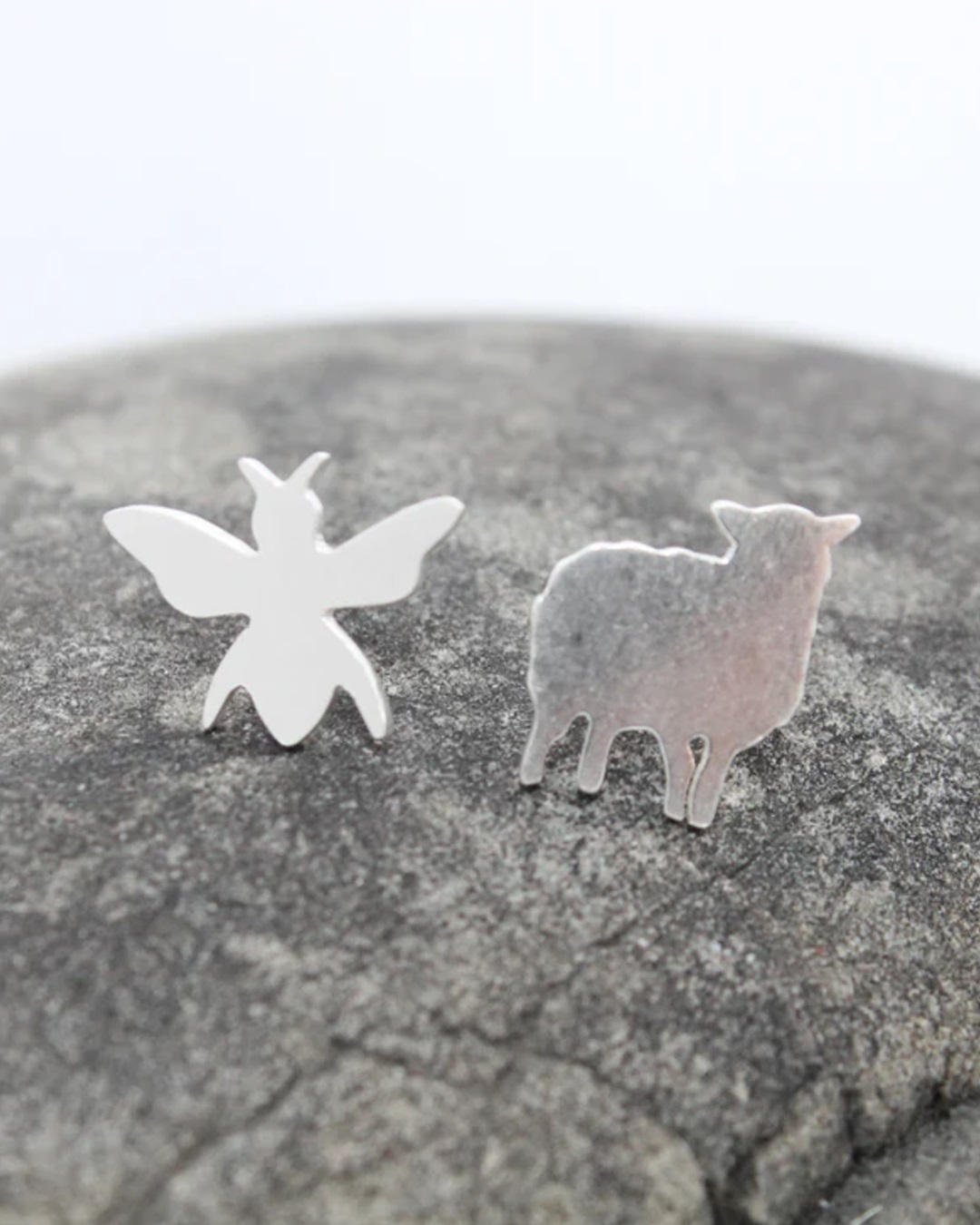 Bee and ewe silver stud earrings on a rock