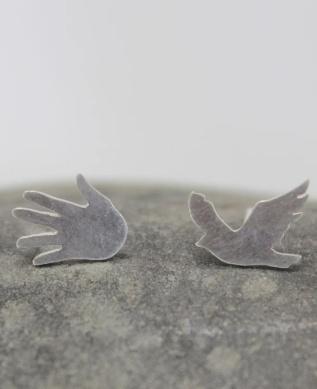 Bird and hand silver earrings on rock
