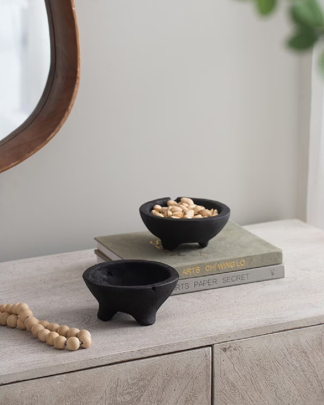Black teak bowls with feet on shelf with nuts in one bowl