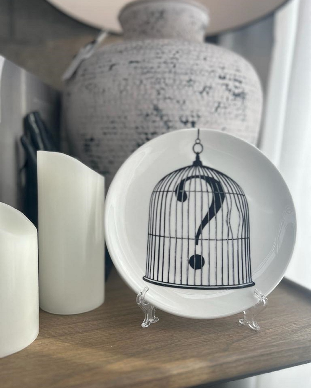 Candles vase and white round plate with bird cage and question mark on it in plate stand