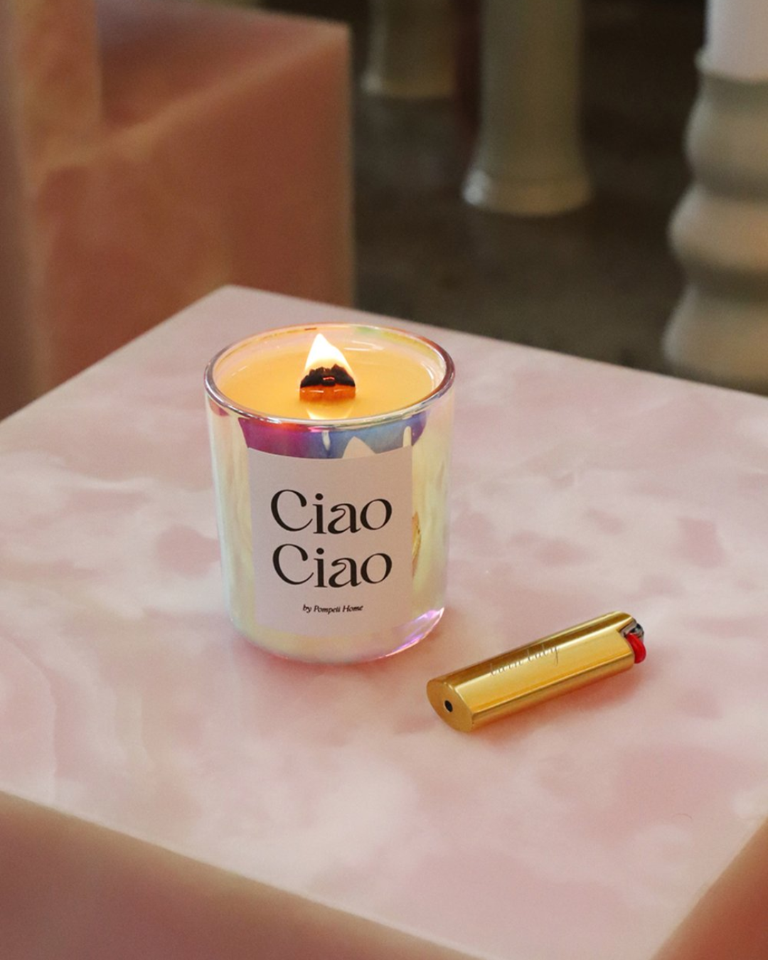 Burning candle in holographic glass jar on pink table with gold lighter holder