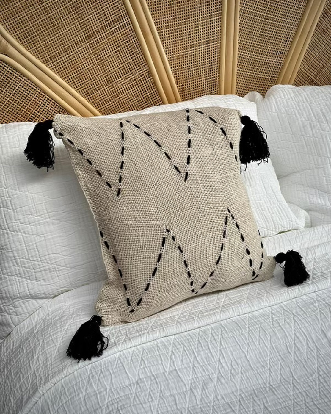 Woven cushion cover with black stitching and tassels on bed