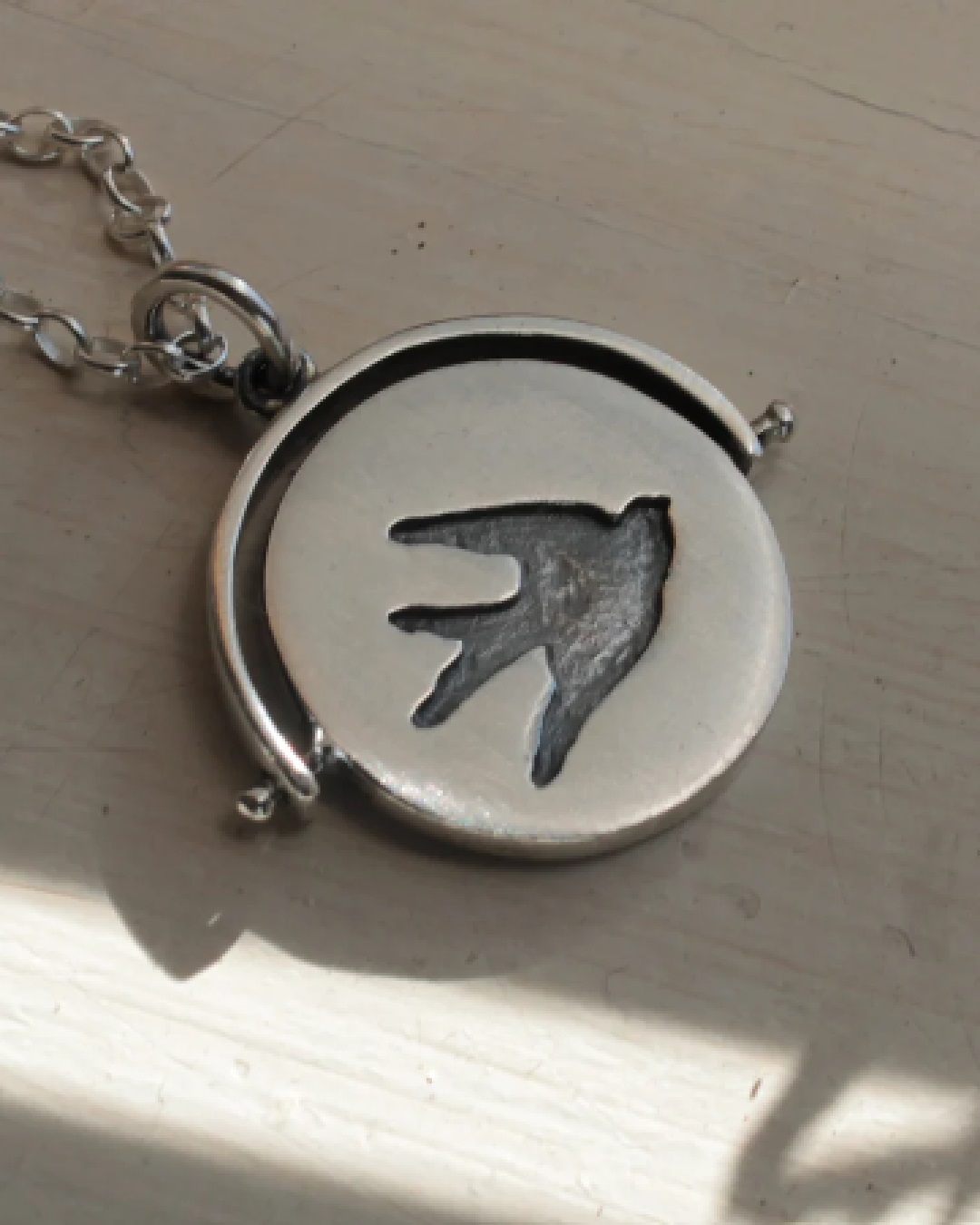 Silver flip circle pendant necklace with a bird