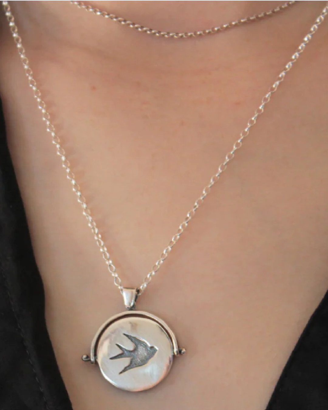 Silver flip circle pendant necklace with a bird on persons neck