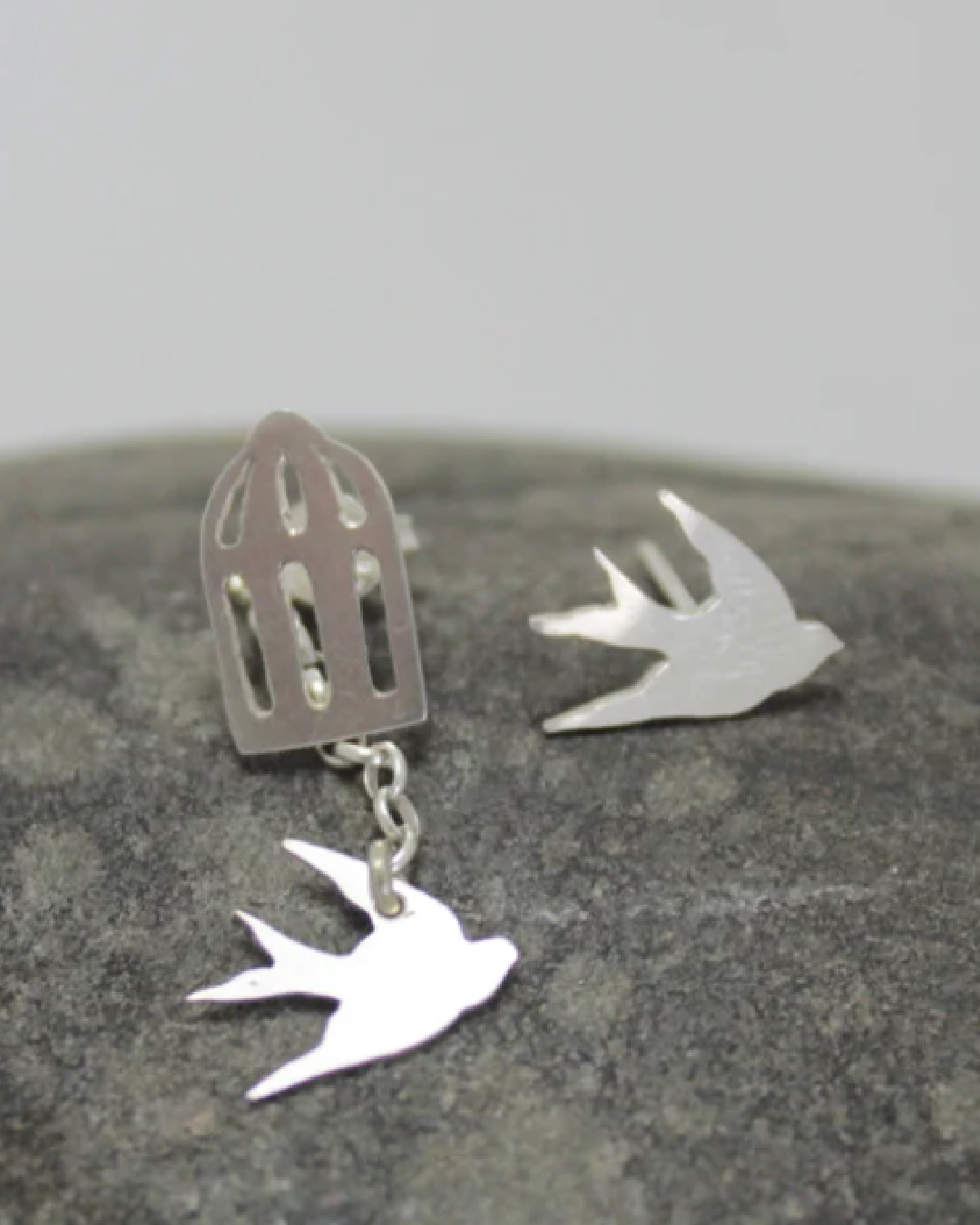 Birds and cage silver earrings on a rock