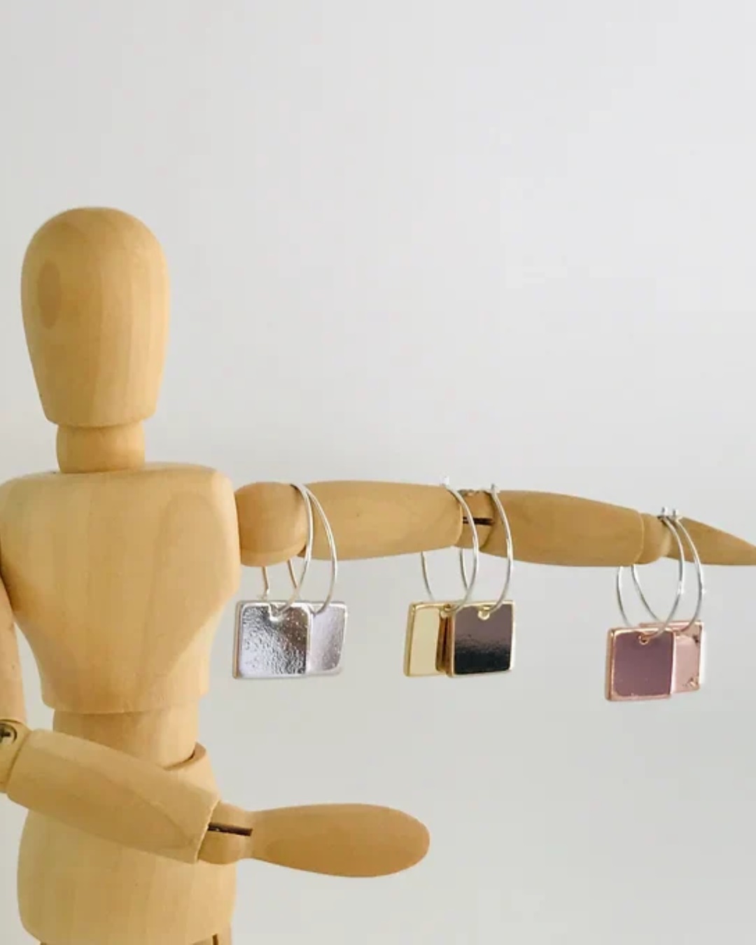 Rose gold, gold and silver square earrings hanging on wooden man arm