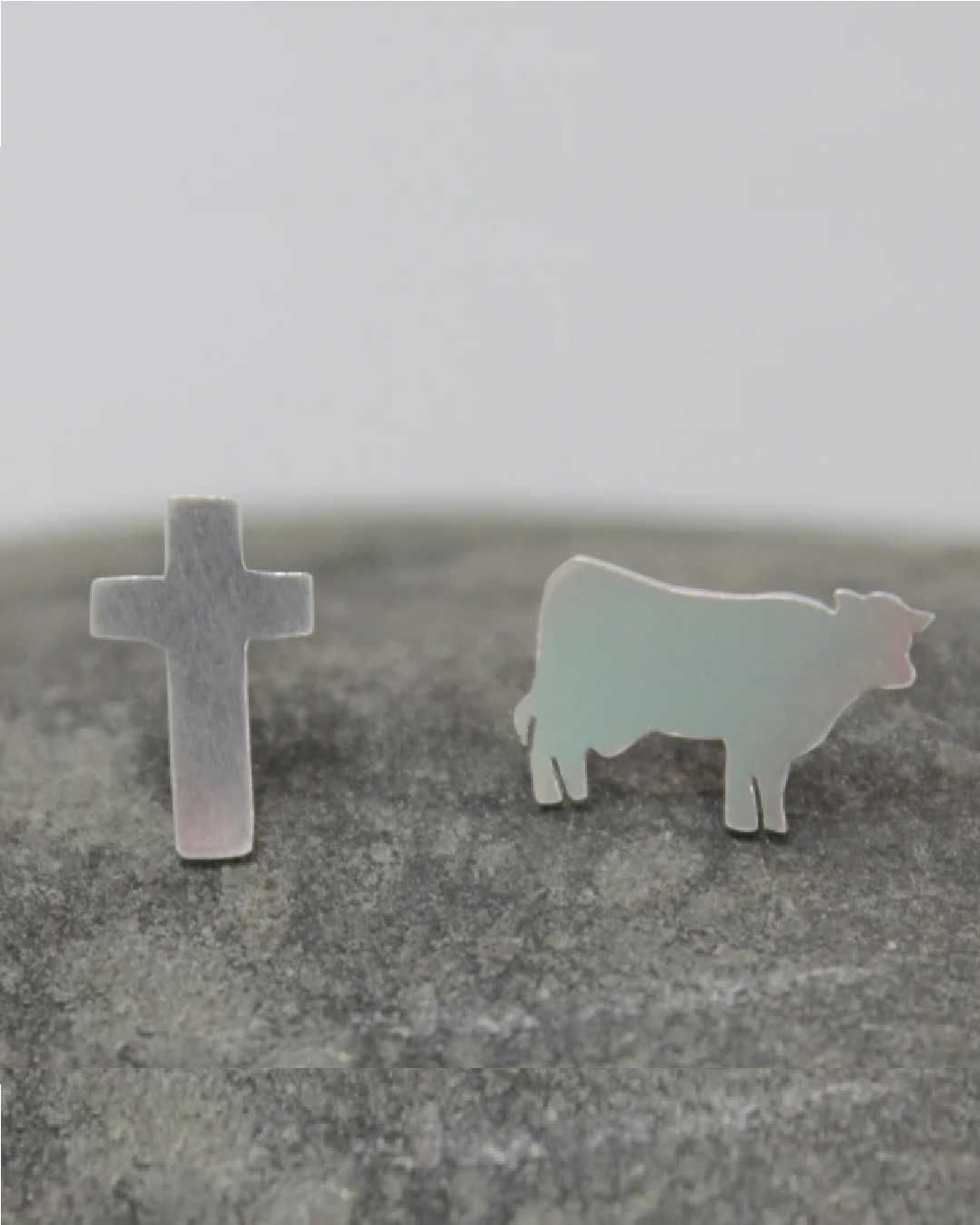 Silver stud earrings one of a cross and one of a cow