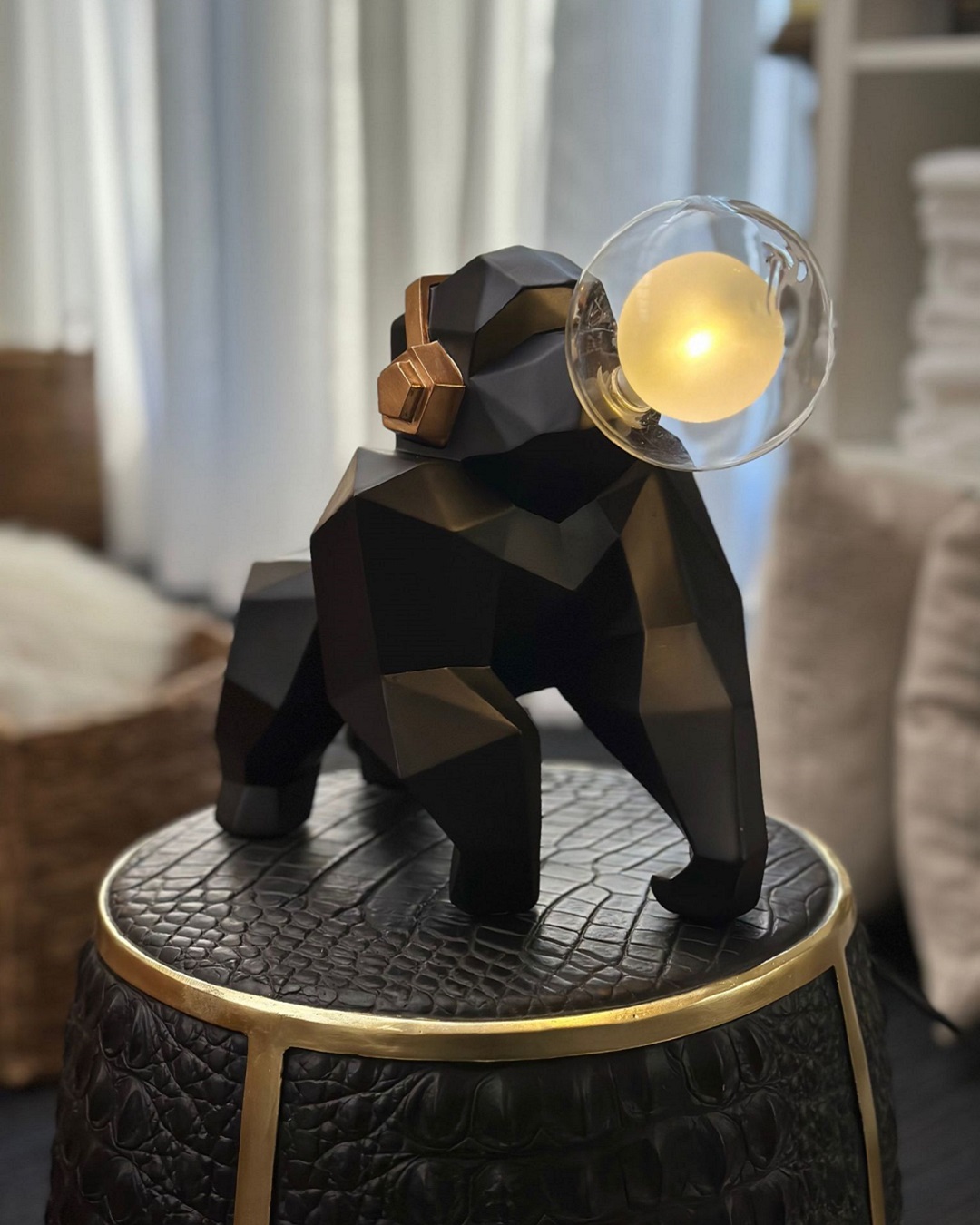 Black gorilla lamp with gold headphones holding a bulb in mouth sitting on black stool
