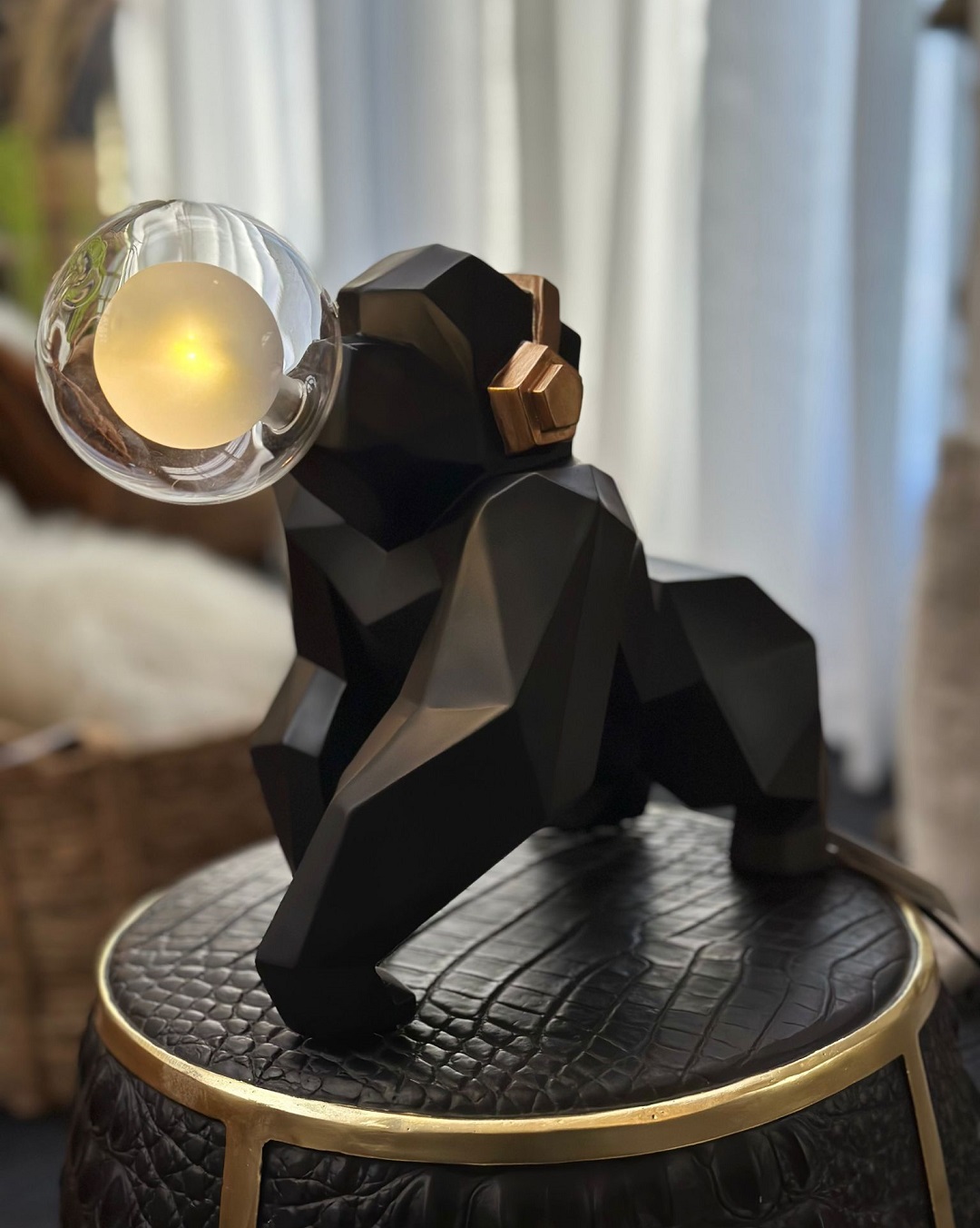 Black gorilla lamp with gold headphones holding a bulb in mouth sitting on black stool
