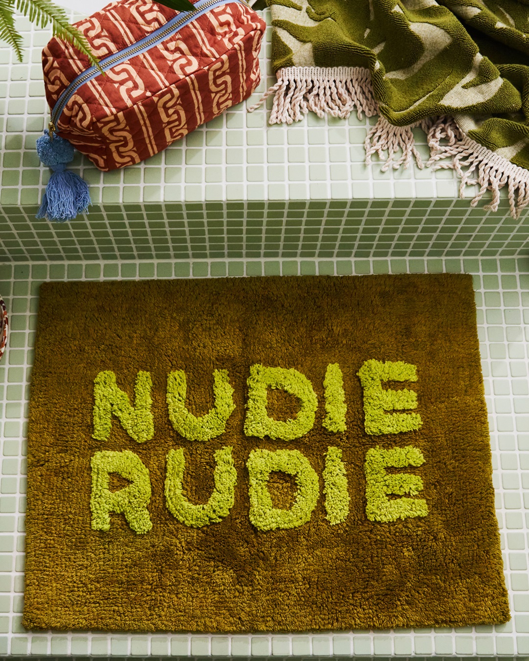 Green artichoke mini bath mat with Nudie Rudie on tiled bathroom floor