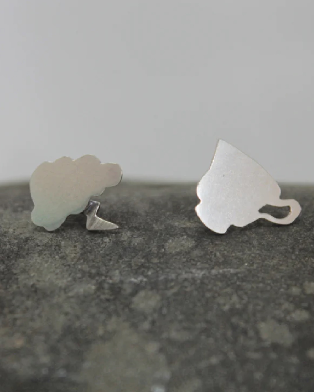 Cloud and teacup silver earrings on a rock