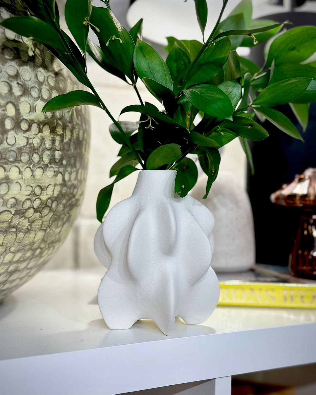 White vase with green foliage on shelf