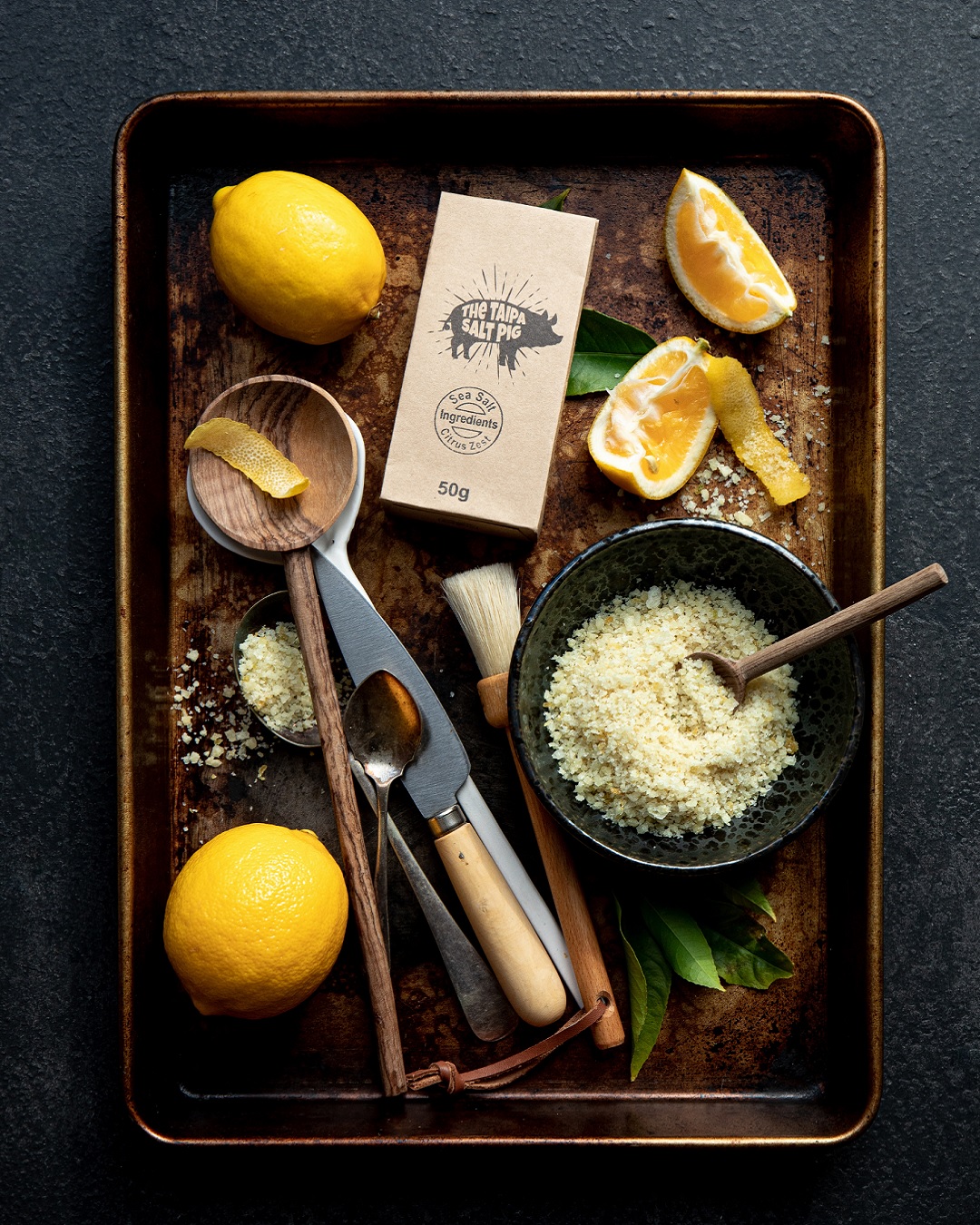 50g bag of Taipa pig citrus salt on tray with lemon, bowl of salt, knives and spoon