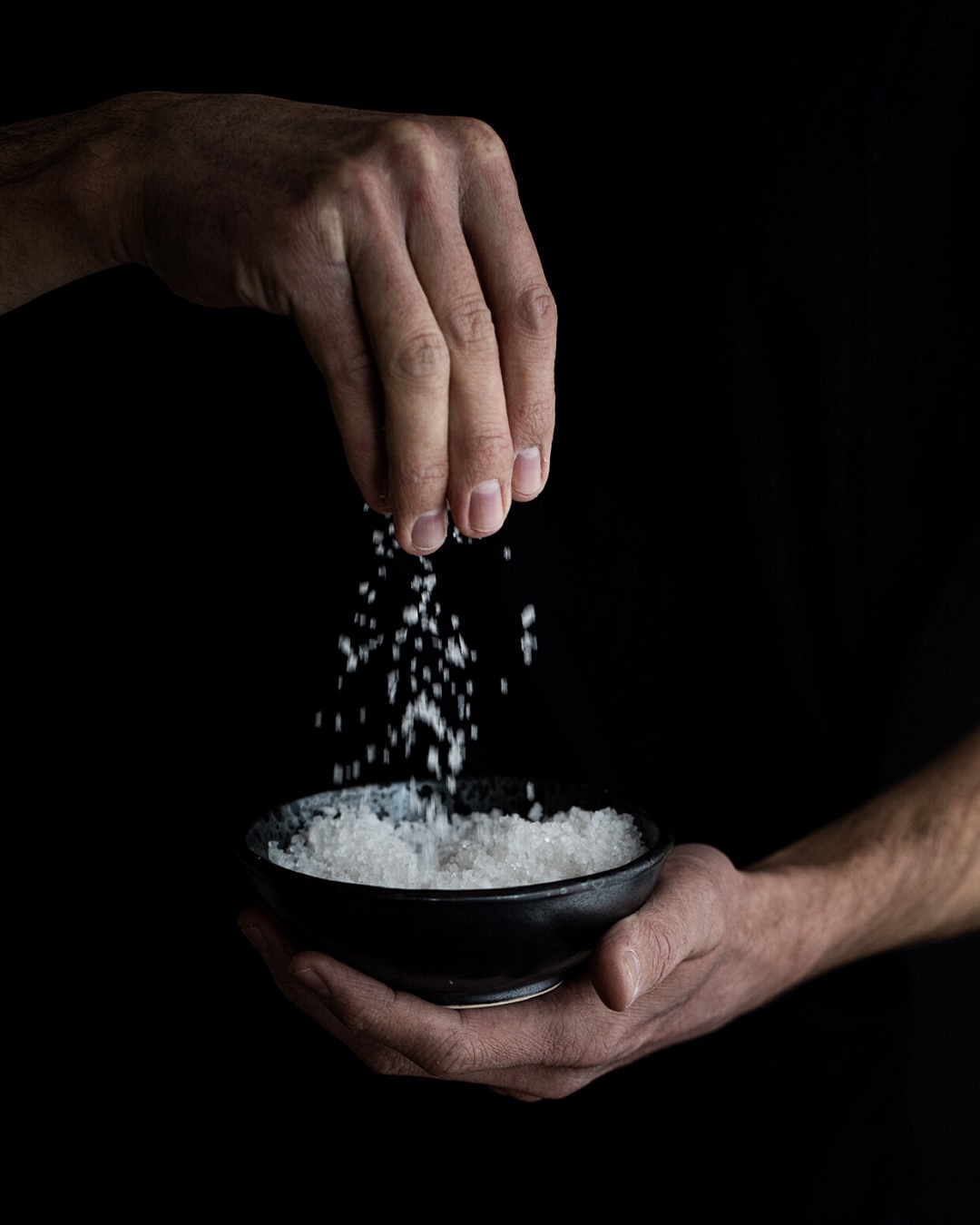 Hand sprinkling salt into a bowl