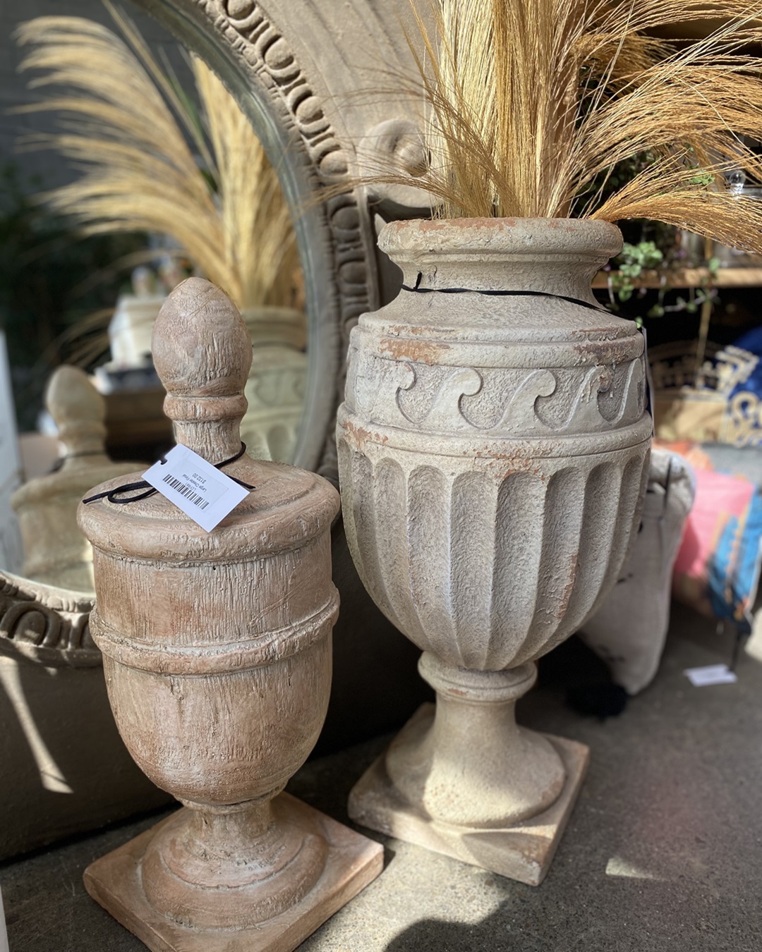 Vintage antique urn with grass in it next to another urn on floor
