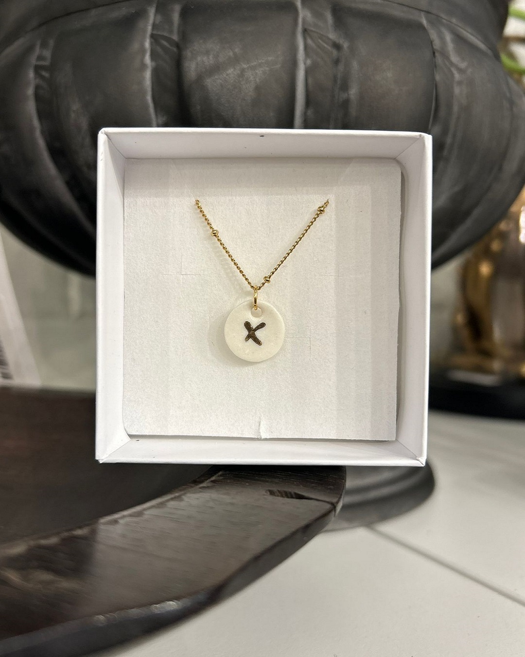 X on white disc necklace hanging in a box
