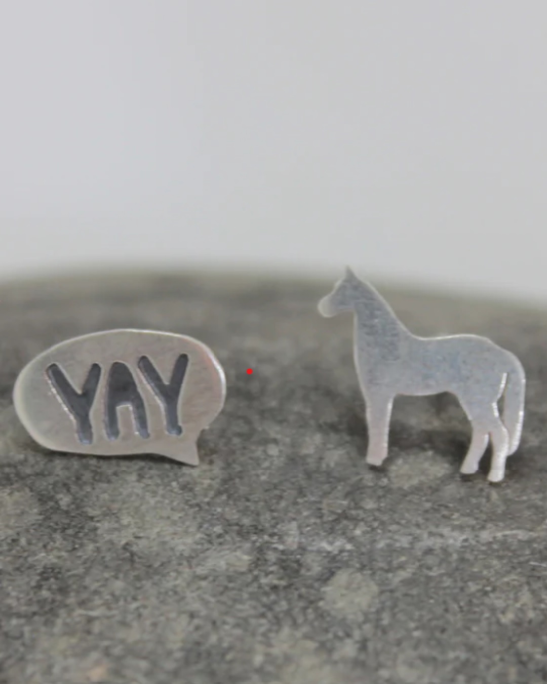 Silver earrings on a rock of a speech mark with yay and a horse