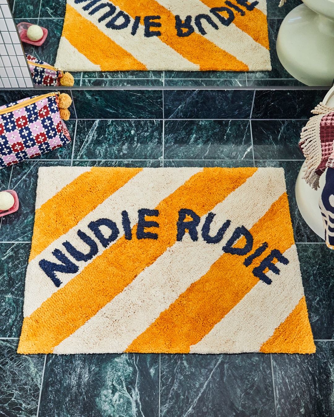 Gold and white stripe bath mat with Nudie Rudie on tiled floor